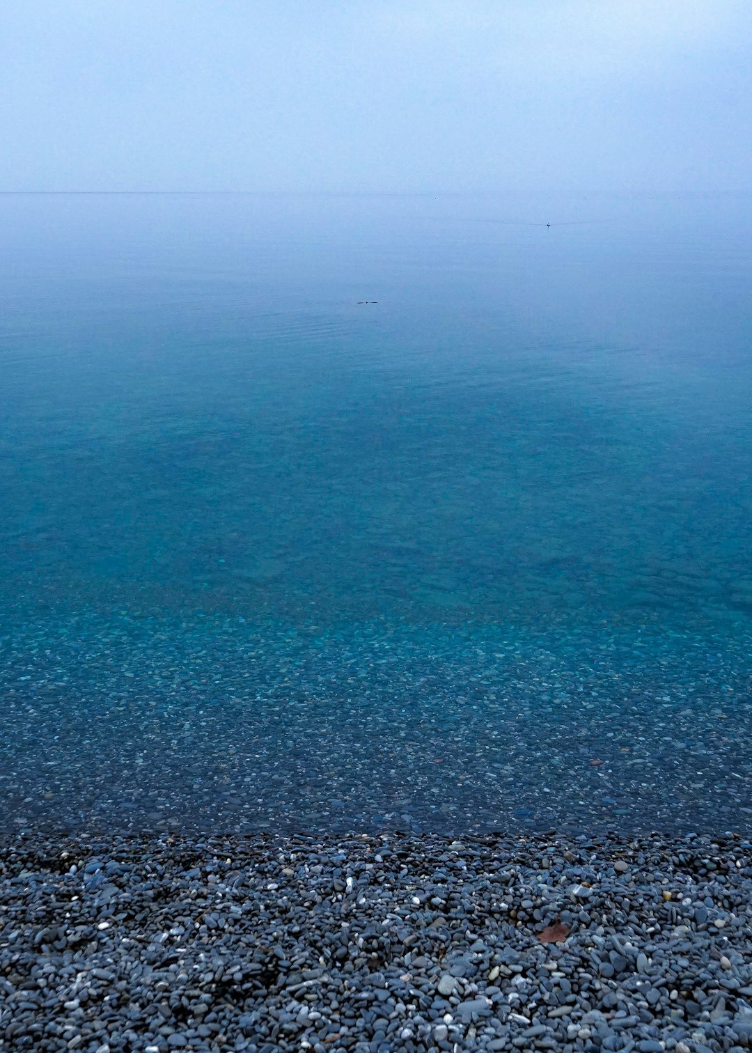 Smooth grey pebbles line the shore by the calm ocean.